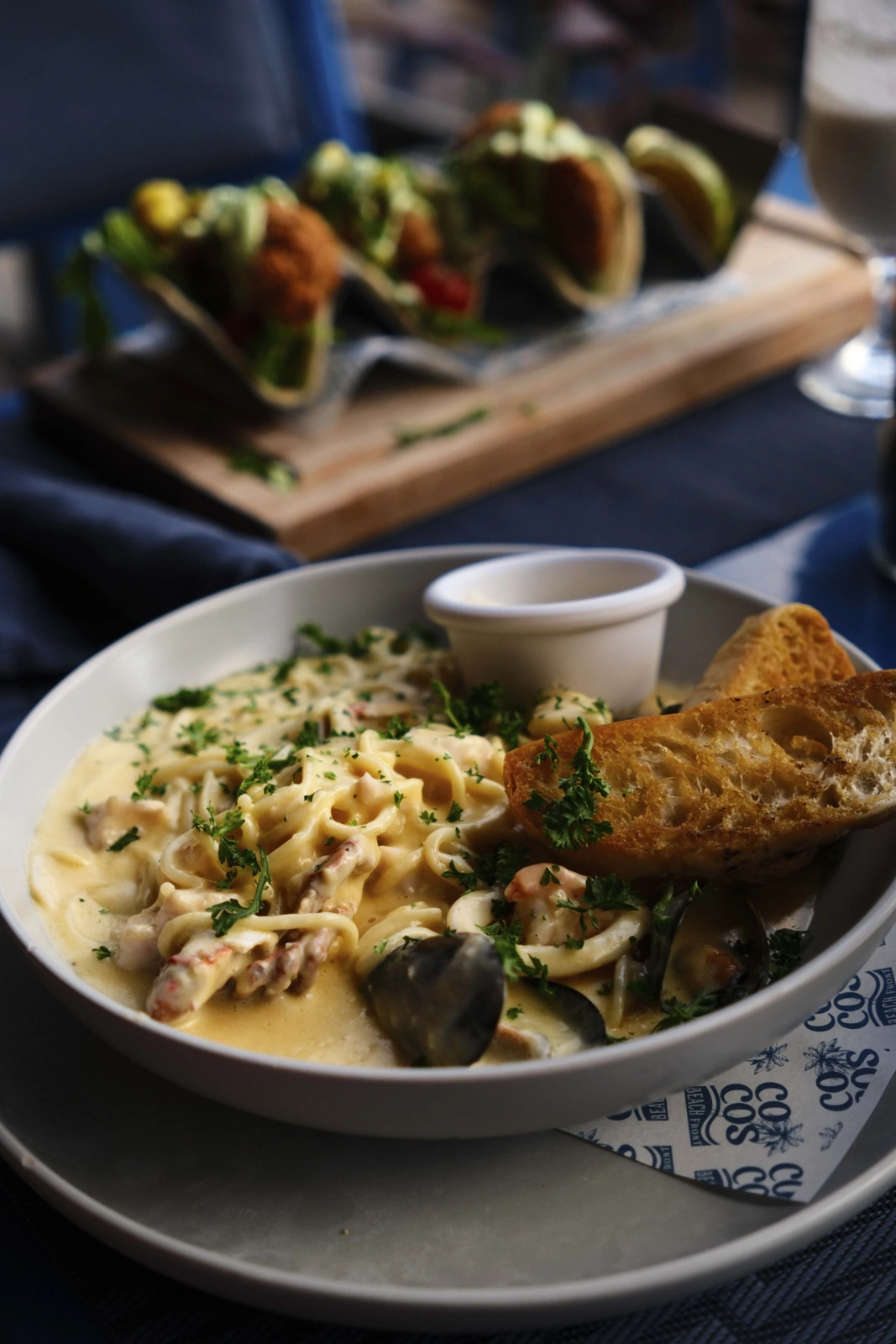 Pasta cremosa con mejillones y tacos de mariscos al fondo en Cocos Beach Front